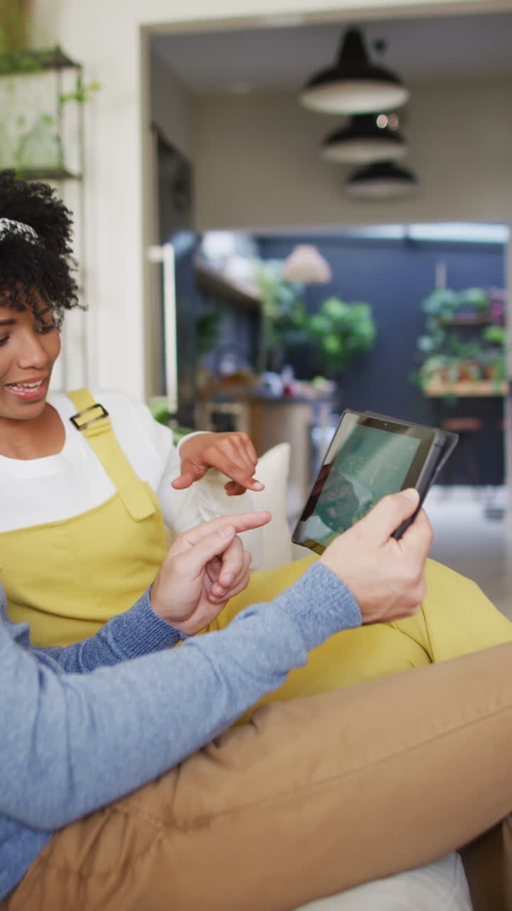 Vertical video of happy diverse couple using smart home interface on tablet at home, copy space