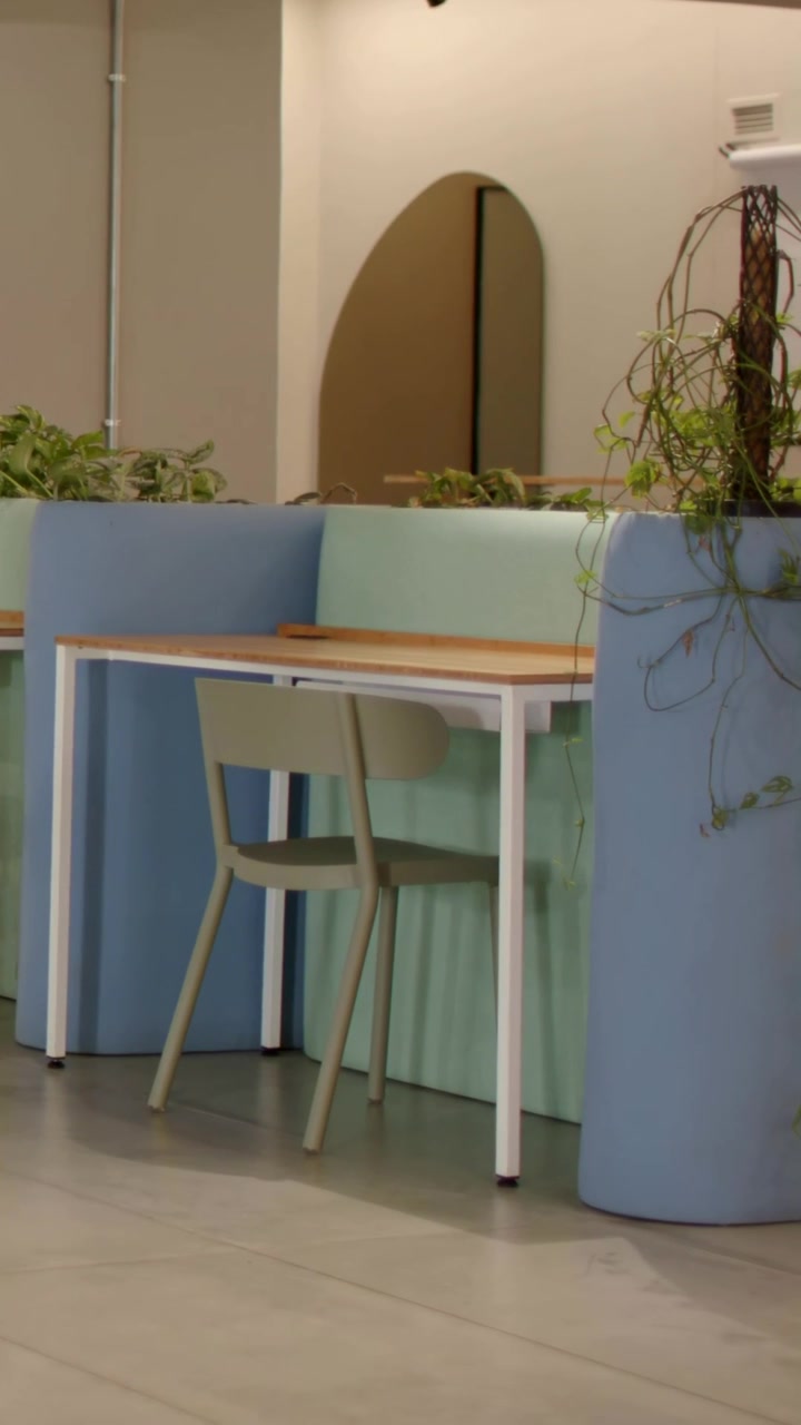 Video vertical: Cámara panorámica revelando una mesa de madera y una silla verde en una sala de descanso de oficina, mostrando enredaderas.