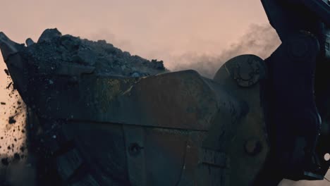 close-up of an excavator bucket digging into a pile of dirt