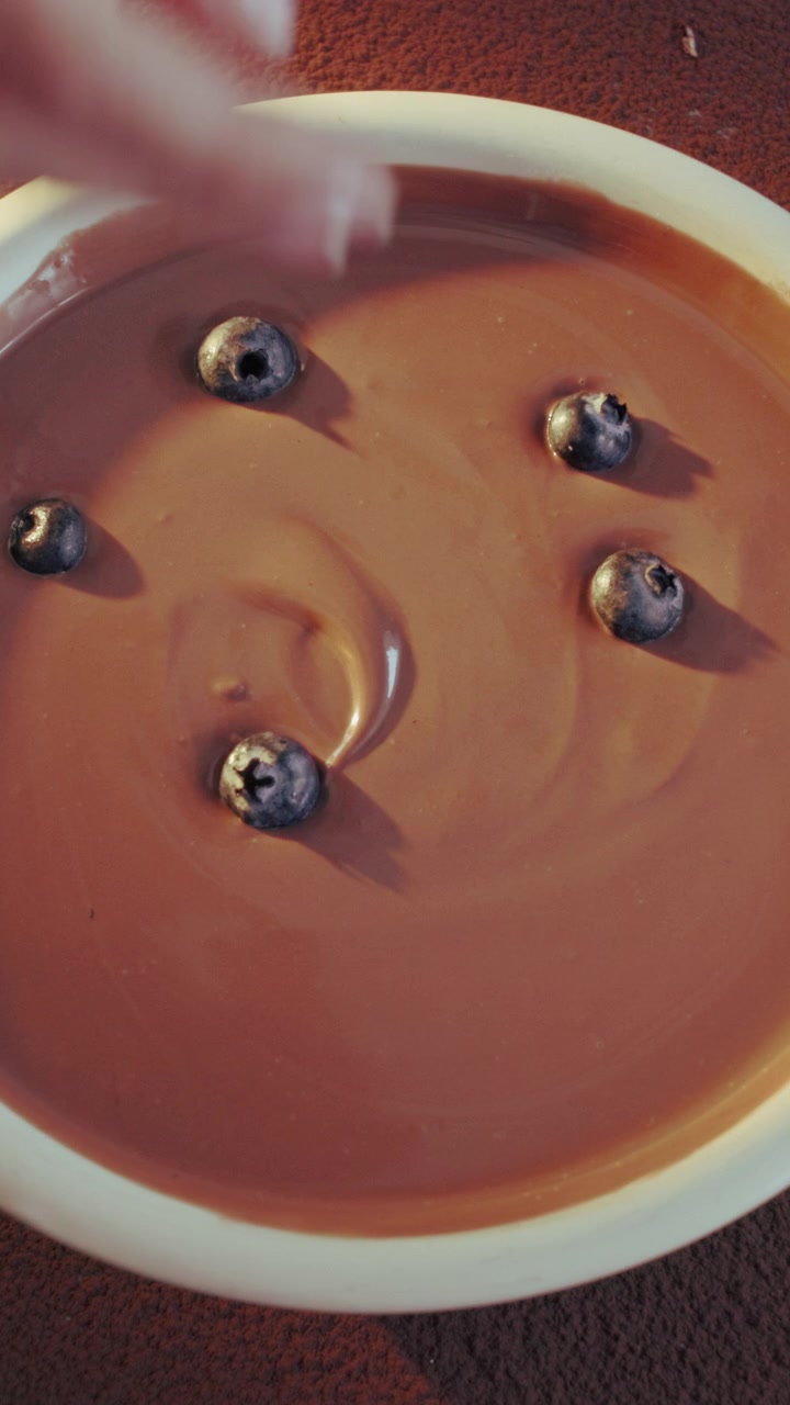 Hand Placing Fresh Blueberries Into A Bowl Of Chocolate Pudding