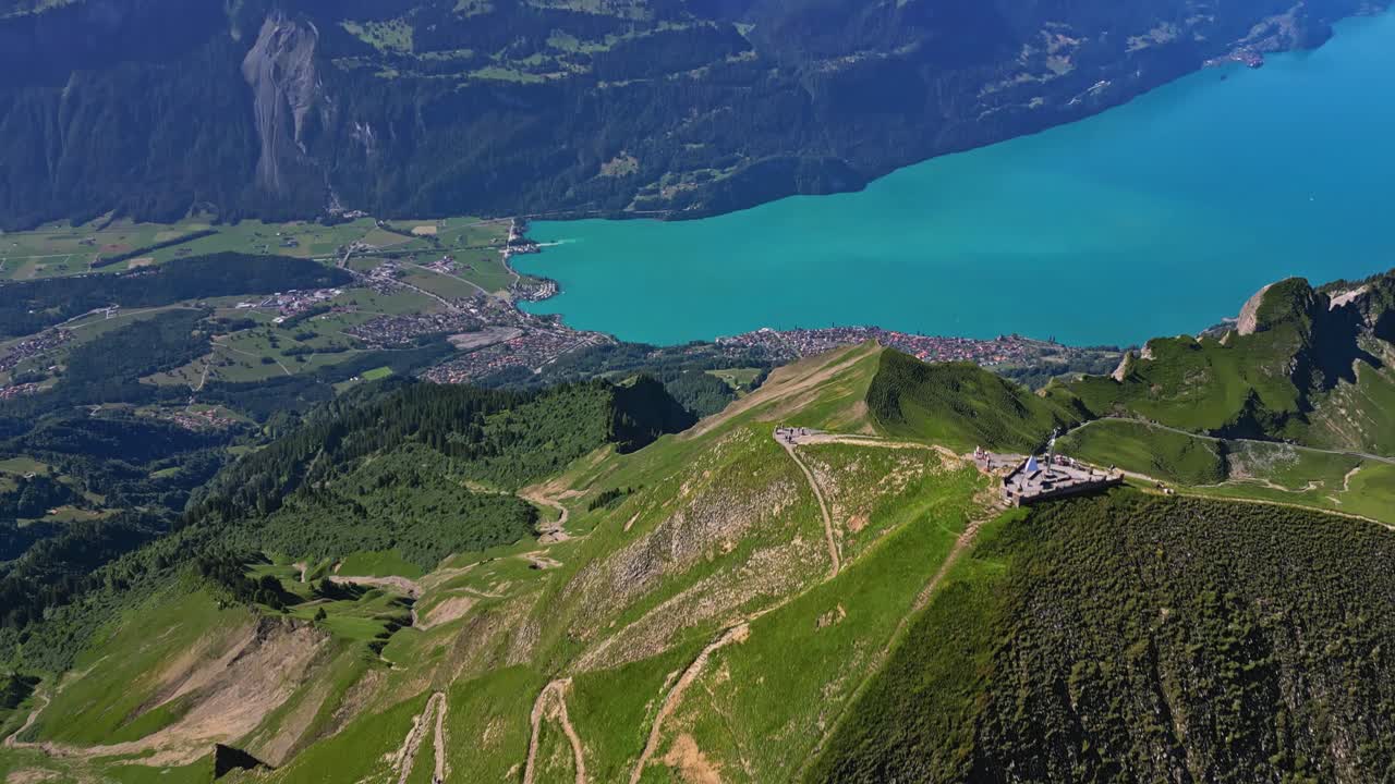 una vista aérea de una cordillera verde, revelando lentamente un lago turquesa y montañas cubiertas de nieve en el fondo