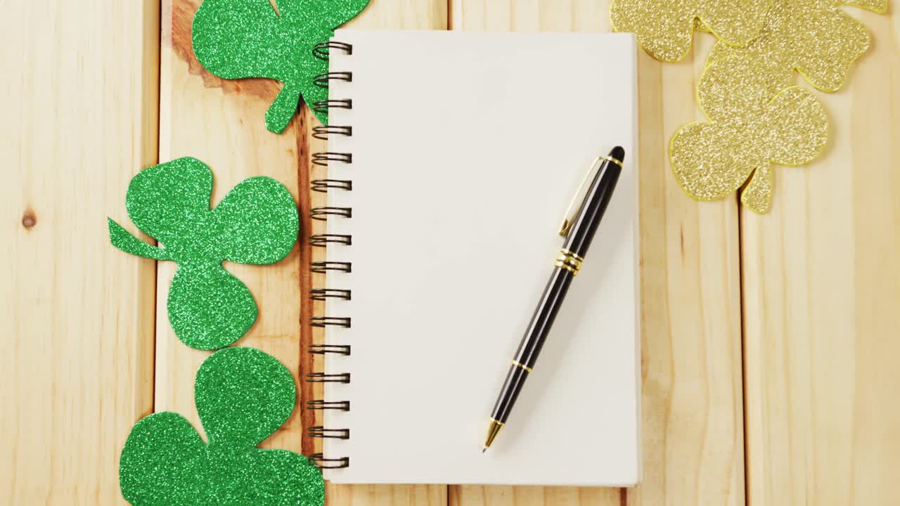 Video of st patrick's green shamrock and notebook with copy space on wooden background