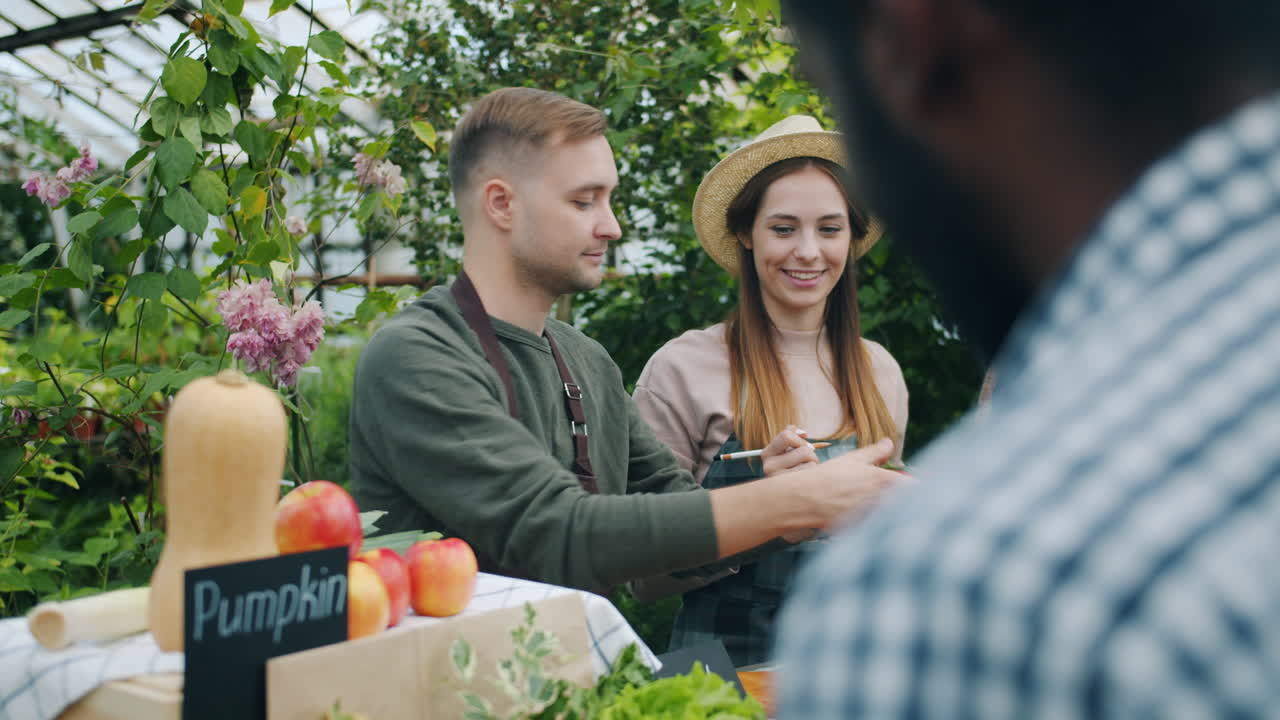 People shopping for produce at a farmers market in a greenhouse