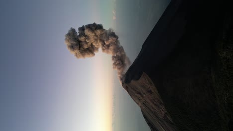 Drone portrait view in Guatemala flying over a volcano crater with an erupting volcano at sunrise surrounded by mist