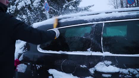 the young man is cleaning car's side window from the snow with a yellow brush in winter