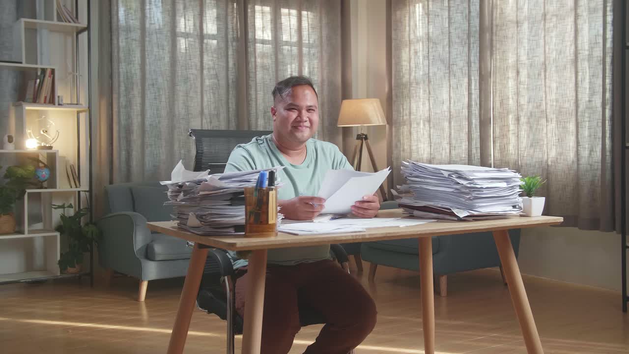 Fat Asian Man Smiling To Camera While Working With Documents At The Office