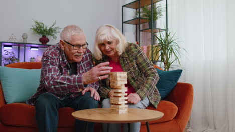 Elderly-old-grandparents-man-woman-playing-in-blocks-wooden-tower-build-board-game-on-table-at-home