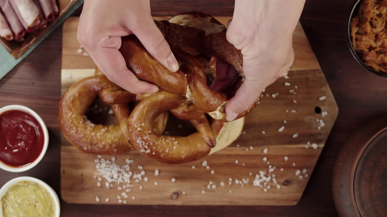 Kädet repimässä vastaleivottua pretzeliä puulaudalla