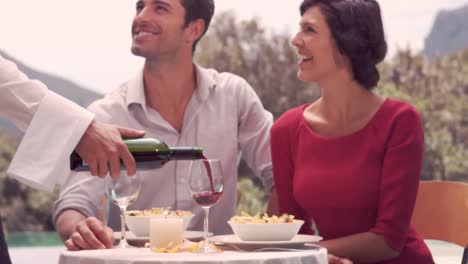 waiter pouring red wine in glass for couple