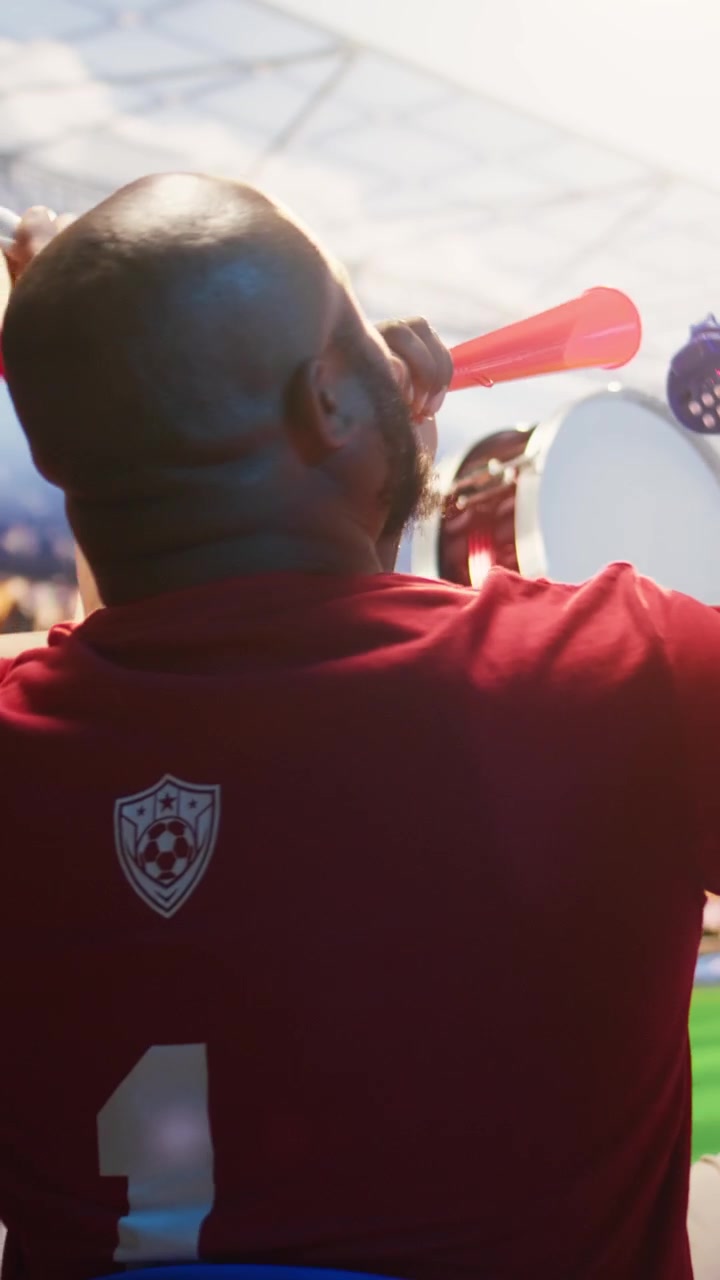 Video verticale. Tifosi con divise da calcio rosse che suonano le vuvuzela durante una partita nello stadio.