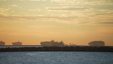 many cargo ships docked and waiting to be unloaded during a global supply chain crisis at sunset