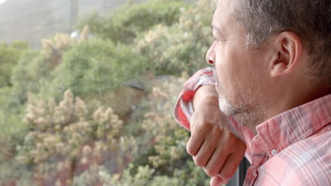 thoughtful senior biracial man looking out of window at countryside, copy space, slow motion