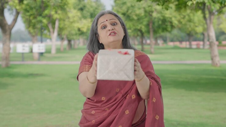 glückliche alte indische frau, die ein geschenk im park gibt