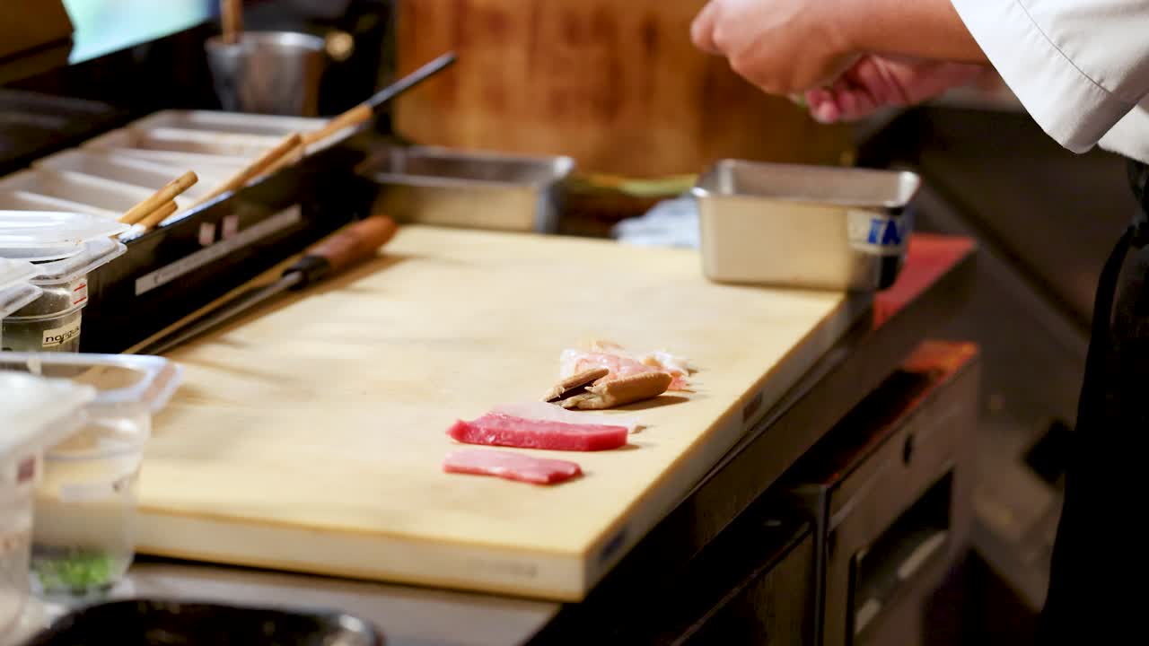 Uno chef professionista dispone del sashimi di tonno fresco su un tagliere di legno nella calda cucina di un ristorante