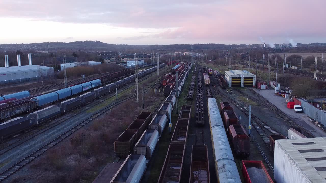 Sunrise aerial view of long railroad tracks with heavy diesel locomotive carriages and cargo container yard low slow forward shot