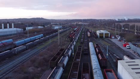 sunrise aerial view of long railroad tracks with heavy diesel locomotive carriages and cargo container yard low slow forward shot