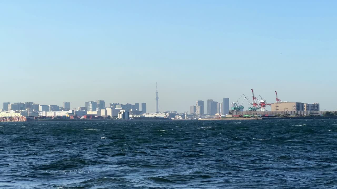 도시 스카이라인과 산업 항구가 걱거리는 파란 바다 물, 은 하늘을 가로질러 볼 수 있습니다.