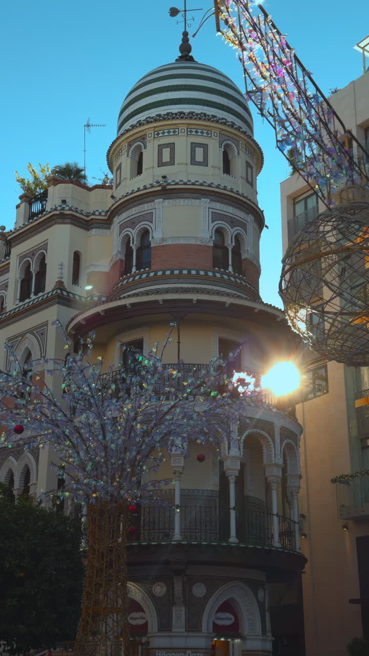 Fachada ornamentada de edifício europeu com decorações douradas, torre com cúpula elevando-se contra o céu azul claro, festivo. Ação