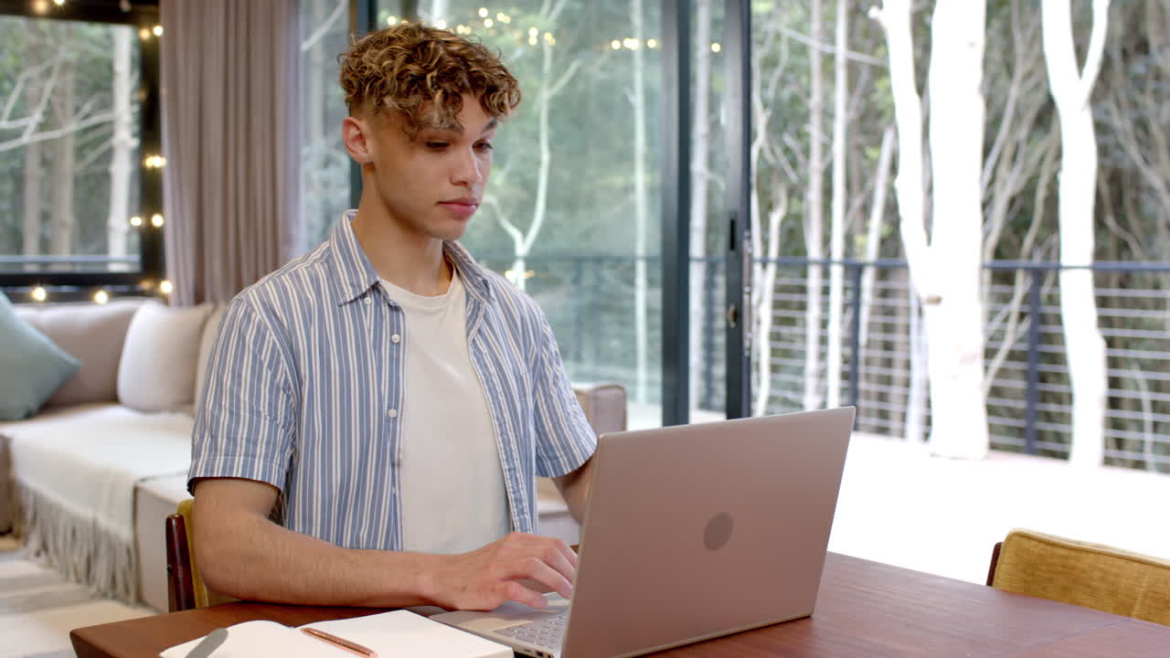 At home, young man using laptop and smiling near window with lights