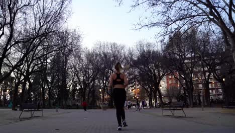 young active female runner jogging in city park from behind, full shot