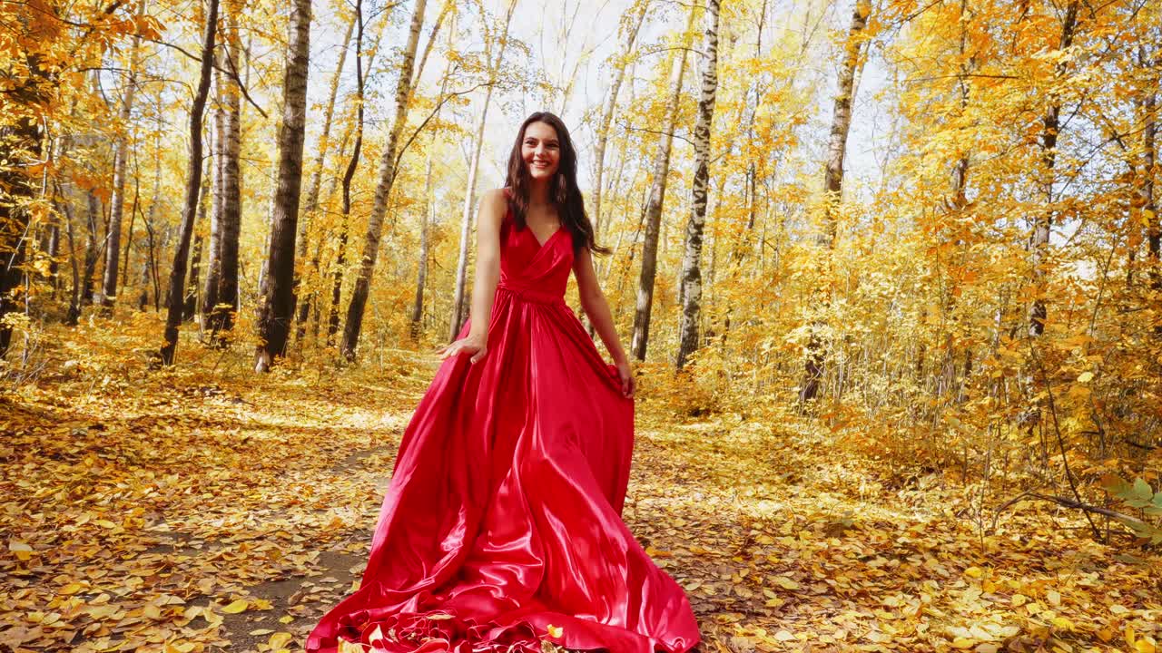 A Graceful Woman in a Flowing Red Dress Strolls Through a Vibrant Autumn Forest Filled with Golden Leaves and Warm Light in the Heart of Nature's Seasonal Transition