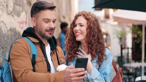 caucasian man with beard and caucasian woman watching something in a smartphone in the street