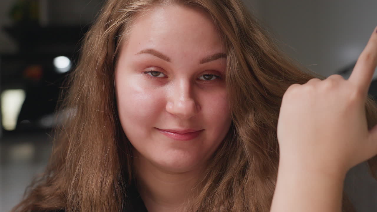 Portrait of beautiful girl smiling while adjusting hair, stylish head turn near camera, kitchen blur, warm daylight on skin, natural expression, hand touch, close view highlighting face
