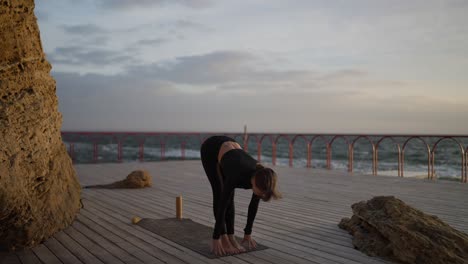 woman practicing yoga by the ocean at sunset