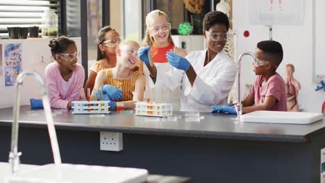 Diverse-female-teacher-and-happy-schoolchildren-having-science-class-in-school-lab