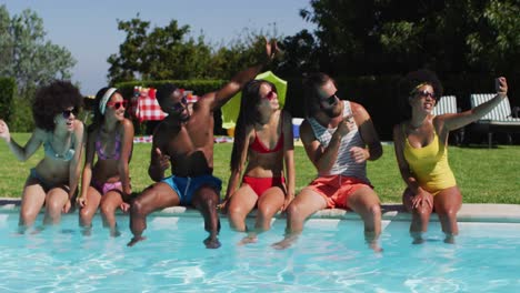 group of diverse friends taking a selfie together on smartphone while sitting by the pool