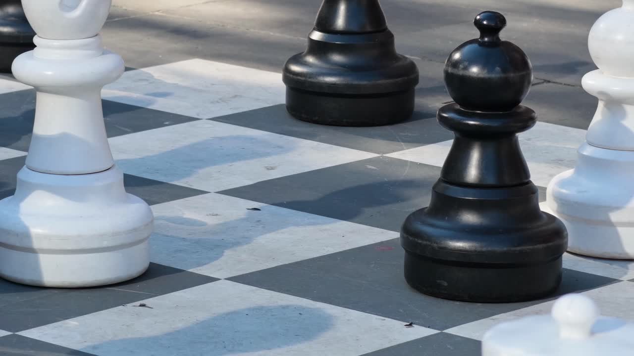 Detailed view of black and white giant chess pieces on an outdoor chessboard.