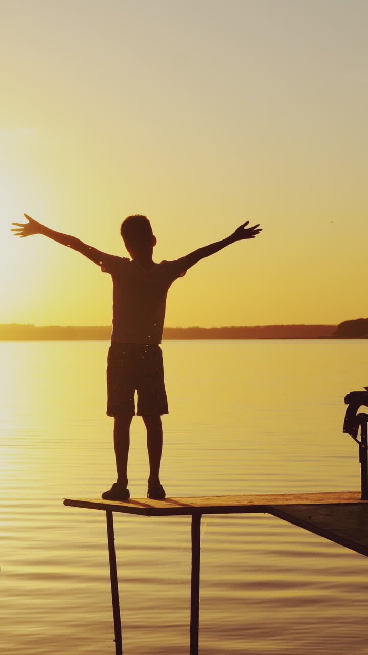 Boy doing yoga exercises by the river at sunset. Silhouette of a boy on an old bridge by the river. Beautiful summer sunset Vertical video
