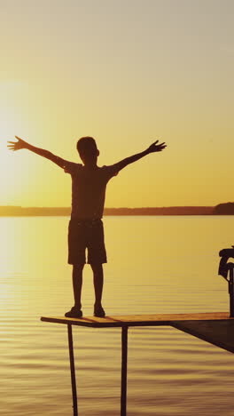 boy doing yoga exercises by the river at sunset. silhouette of a boy on an old bridge by the river. beautiful summer sunset vertical video