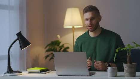 Un-Hombre-Guapo-Se-Comunica-Por-Video-Chat-Con-Una-Computadora-Portátil-Sonriendo-Y-Gesticulando-Mirando-La-Pantalla-Sentado-En-Casa-Por-La-Noche