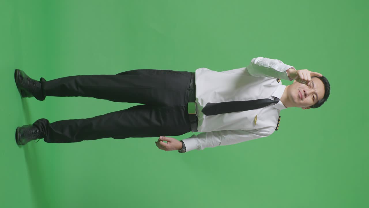 아시아 남성 조종사가 웃고 가을 만지며 녹색 스크린 배경 스튜디오에 서있는 동안 당신을 가리키고 있습니다.