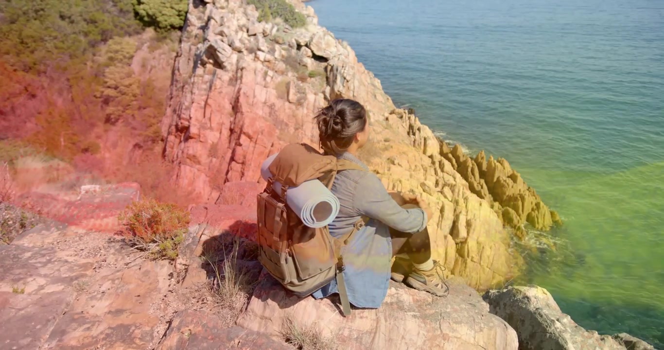 Mujer ajustando su pose al borde del acantilado desencadena ondas tecnológicas que se extienden por la vista al mar, evocando una brisa.