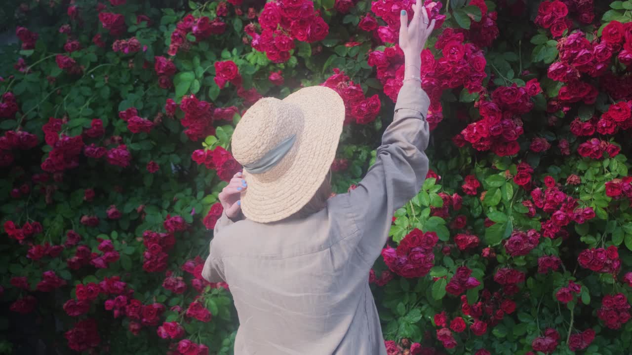 모자 를 입은 여자 정원사 가 정원 에서 자란 장미 를 새 를 맡는다