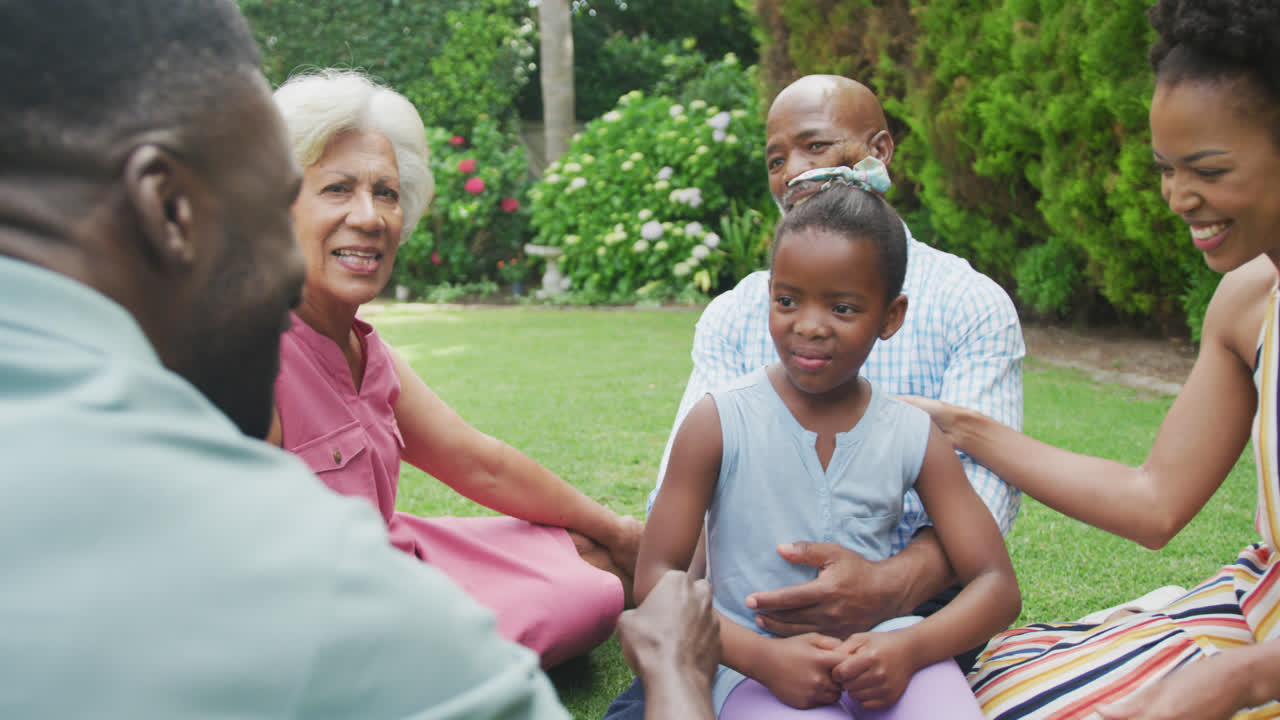 Happy african american family sitting, talking and playing in garden