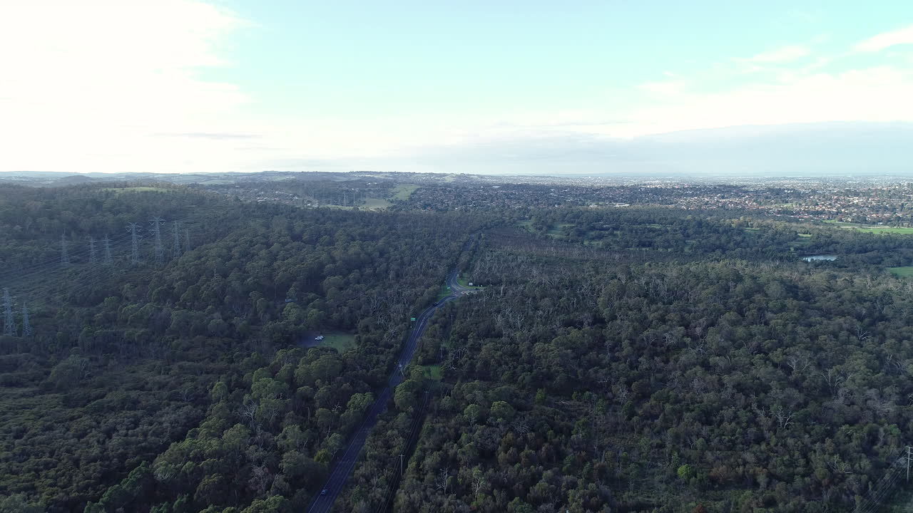 Smooth tracking hyperlapse following traffic moving between a forested area which connects suburban regions of a much large surrounding city.