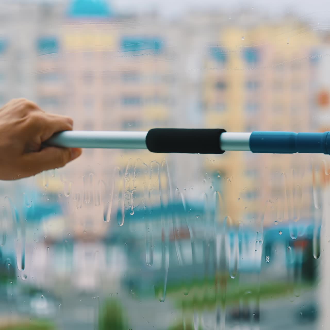 Hand with a cleaning brush is washing window. Plastic window cleaning from outside of a high rise building in the city. View from flat