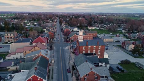 a drone approaching view of a small town and a steeple at sunrise as it gets ready to break the horizon, with orange and reds on a spring sunrise with partial cloudy skies