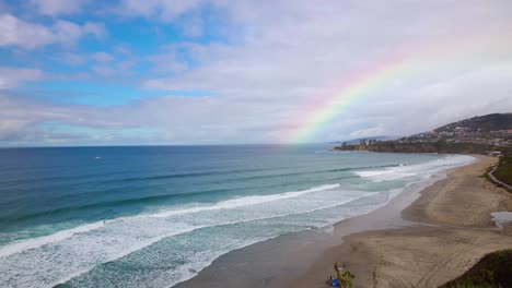 Un-Hermoso-Lapso-De-Tiempo-De-4k-Desde-El-Acantilado-De-Una-Playa-De-Dana-Point-California-Justo-Después-De-Que-Lloviera-Con-Un-Arco-Iris-En-El-Fondo-Mientras-Los-Surfistas-Navegan-Y-Las-Familias-Disfrutan-De-Un-Día-Soleado-De-Vacaciones