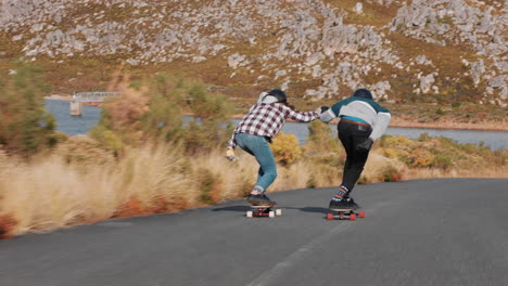 Jóvenes-Amigos-Practicando-Longboard-Juntos-Tomados-De-La-Mano-Navegando-Cuesta-Abajo-Corriendo-Adolescentes-Felices-Disfrutando-Montando-Patineta-En-La-Hermosa-Vista-Trasera-De-La-Carretera-Rural