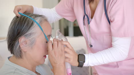 nurse assisting senior asian woman with oxygen mask during home healthcare visit