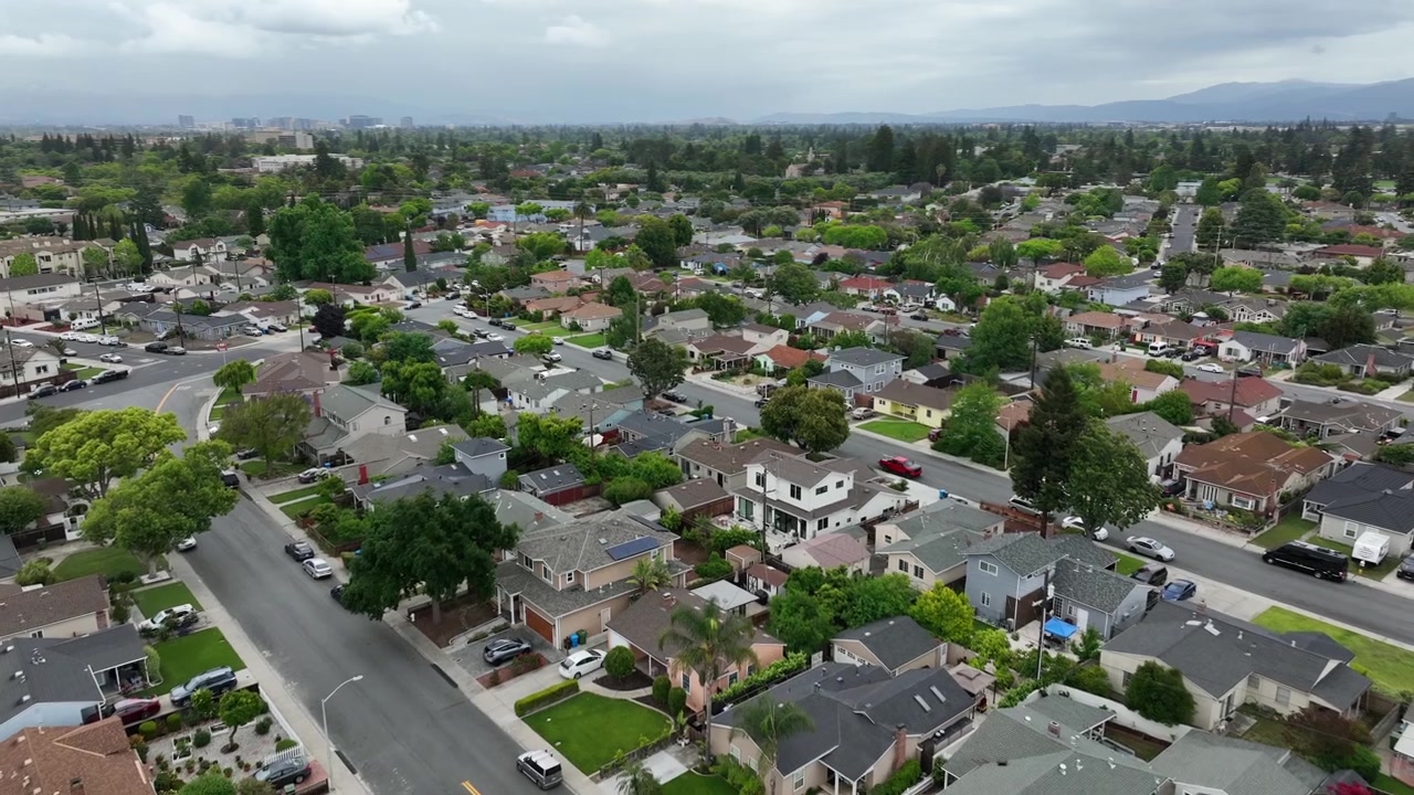 Vasto bairro suburbano de casas e ruas sinuosas preenche as planícies do Vale do Silício com uma cordilheira distante sob céus nublados em Santa Clara, Califórnia, EUA. Filmagem aérea de drone