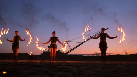 professional artists show a fire show at a summer festival on the sand in slow motion. fourth person acrobats from circus work with fire at night on the beach.