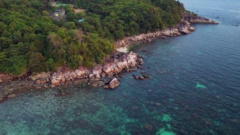 Capturing-the-beauty-of-a-tropical-island,-turquoise-waters-and-rocky-coastline,-this-aerial-view-shows-vibrant-blue-and-green-hues-against-rugged-cliffs-and-shores