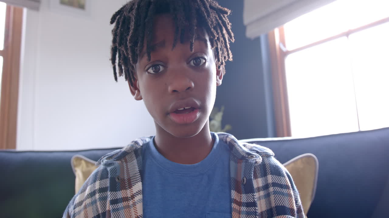 Ragazzo afroamericano seduto sul divano che fa una videochiamata a casa, slow motion