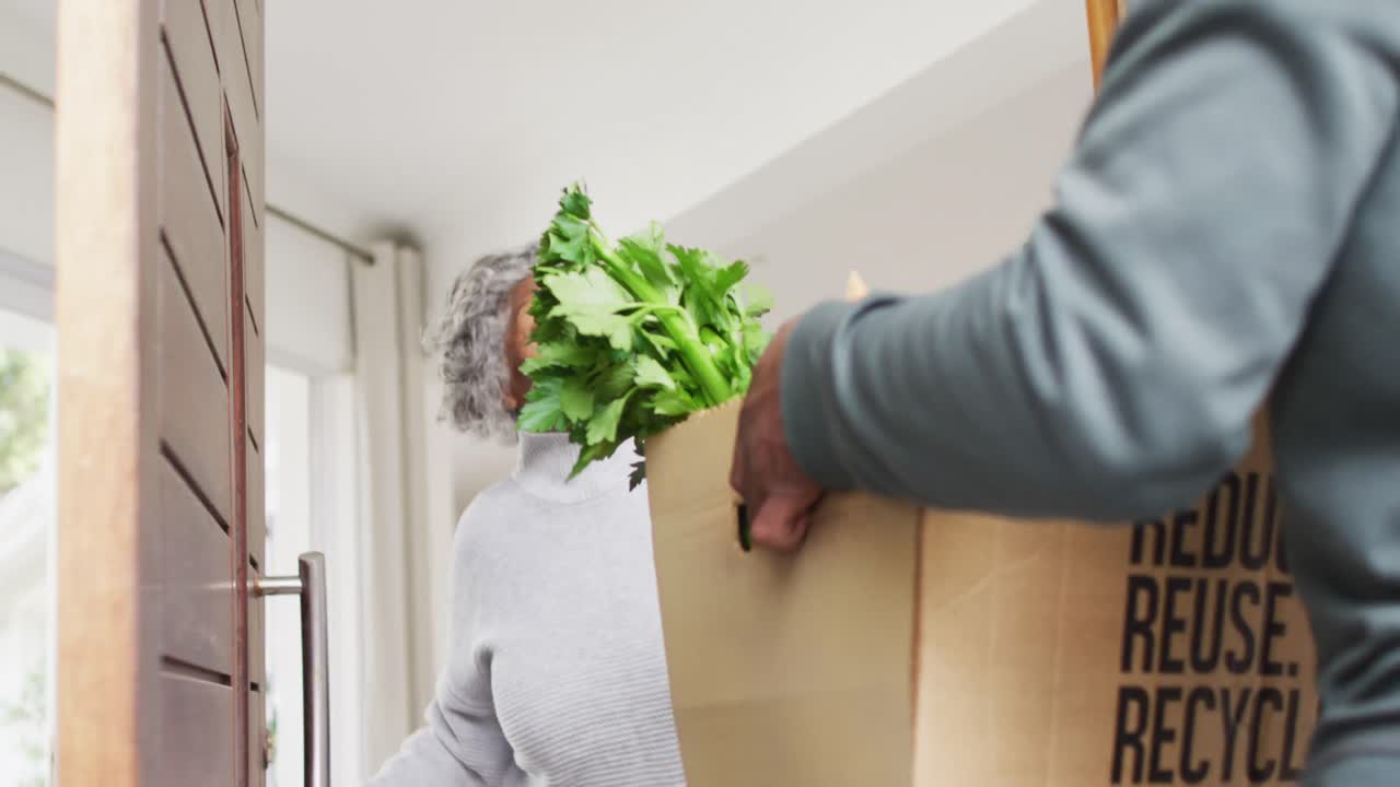 행복한 노인 아프리카계 미국인 여성이 배달사로부터 식료품을 받고 있습니다.