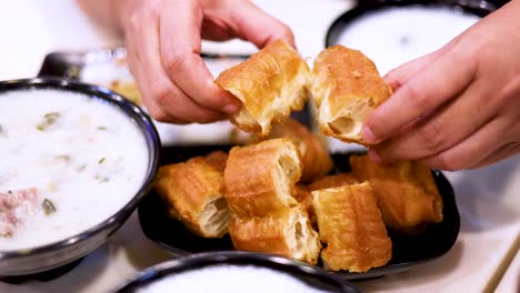manos rompiendo masa frita sobre cuencos de congee